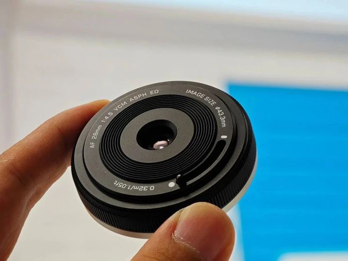 Ультракомпактний об'єктив Viltrox AF 28mm f/4.5 Chip у повнокадровій версії лежить у пальцях руки, видно ребристе металеве кільце та важіль шторки перед виходом на вуличну прогулянку